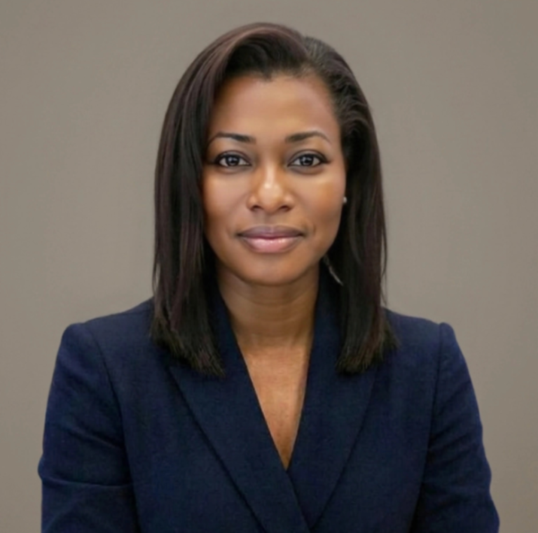 Professional portrait of a woman in a navy blazer with a belt, seated against a neutral gray background.