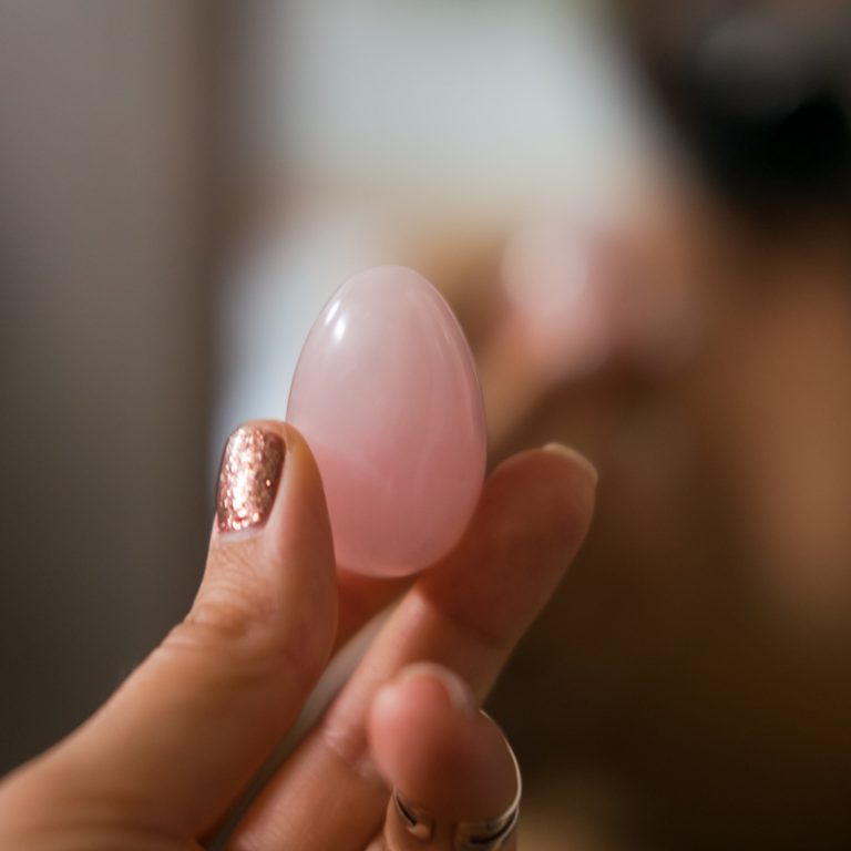 Woman holding in hand a vaginal (yoni) egg. Rose quartz healing crystal egg. Feminine energy concept