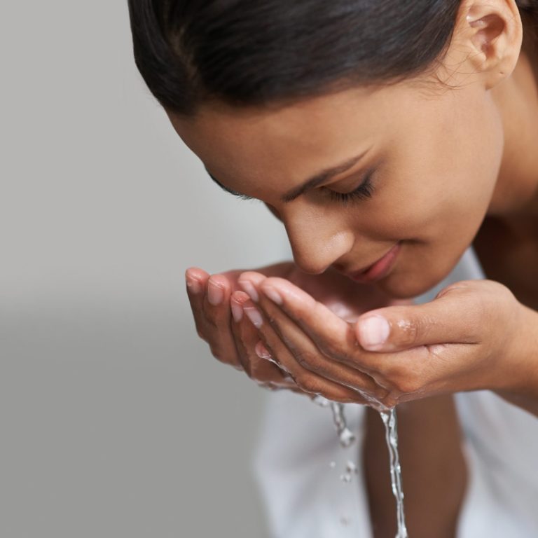 Shot of a young woman washing her face at the basin.